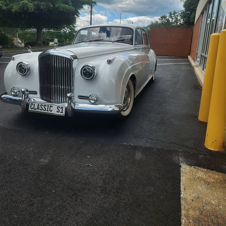 Before: a white vintage car in a parking lot with trees, power lines and a building all sharp behind it
