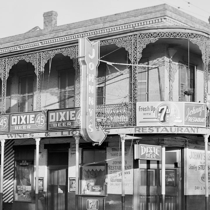 Before: a black and white photograph from 1940 of a restaurant on a street corner with iron balconies and signs
